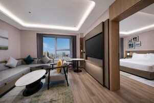 Una habitación de hotel moderna con un sofá, una mesa de comedor, una cama y un televisor grande.