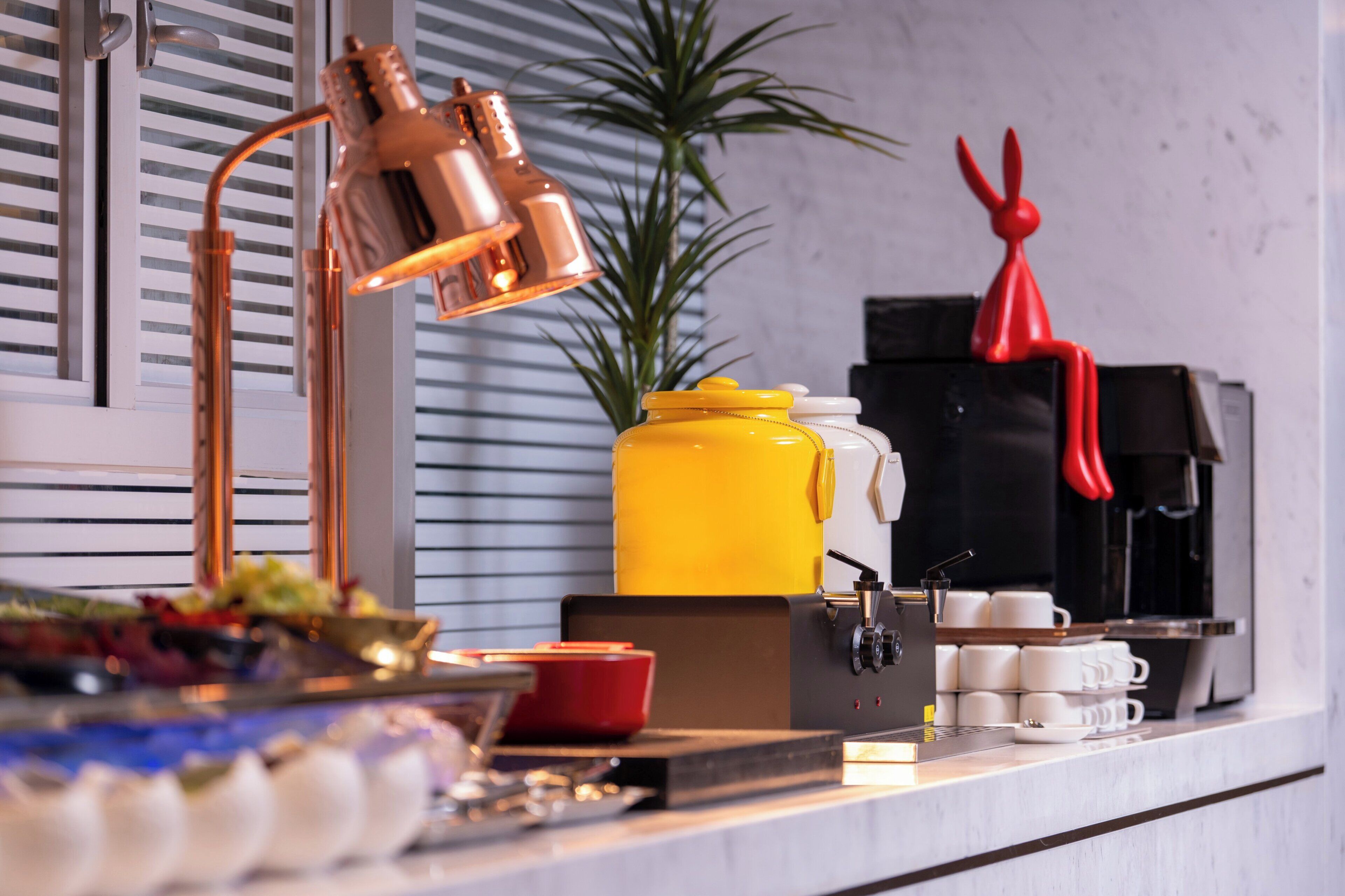 Una encimera de cocina con una cafetera, un florero amarillo y un adorno rojo.