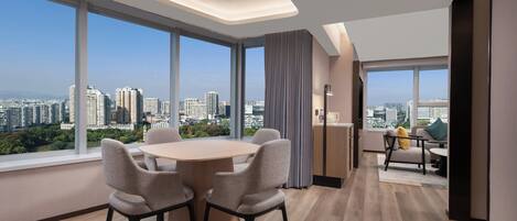 Una habitación de hotel moderna con un amplio comedor, asientos cómodos y vistas a la ciudad a través de ventanas panorámicas.