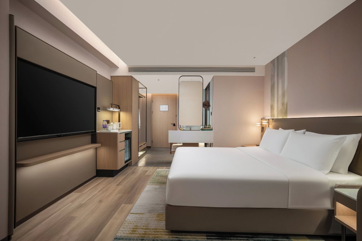 Une chambre d’hôtel moderne dotée d’un grand lit, d’une télévision à écran plat, d’un bureau et d’une salle de bain avec un miroir et un lavabo.