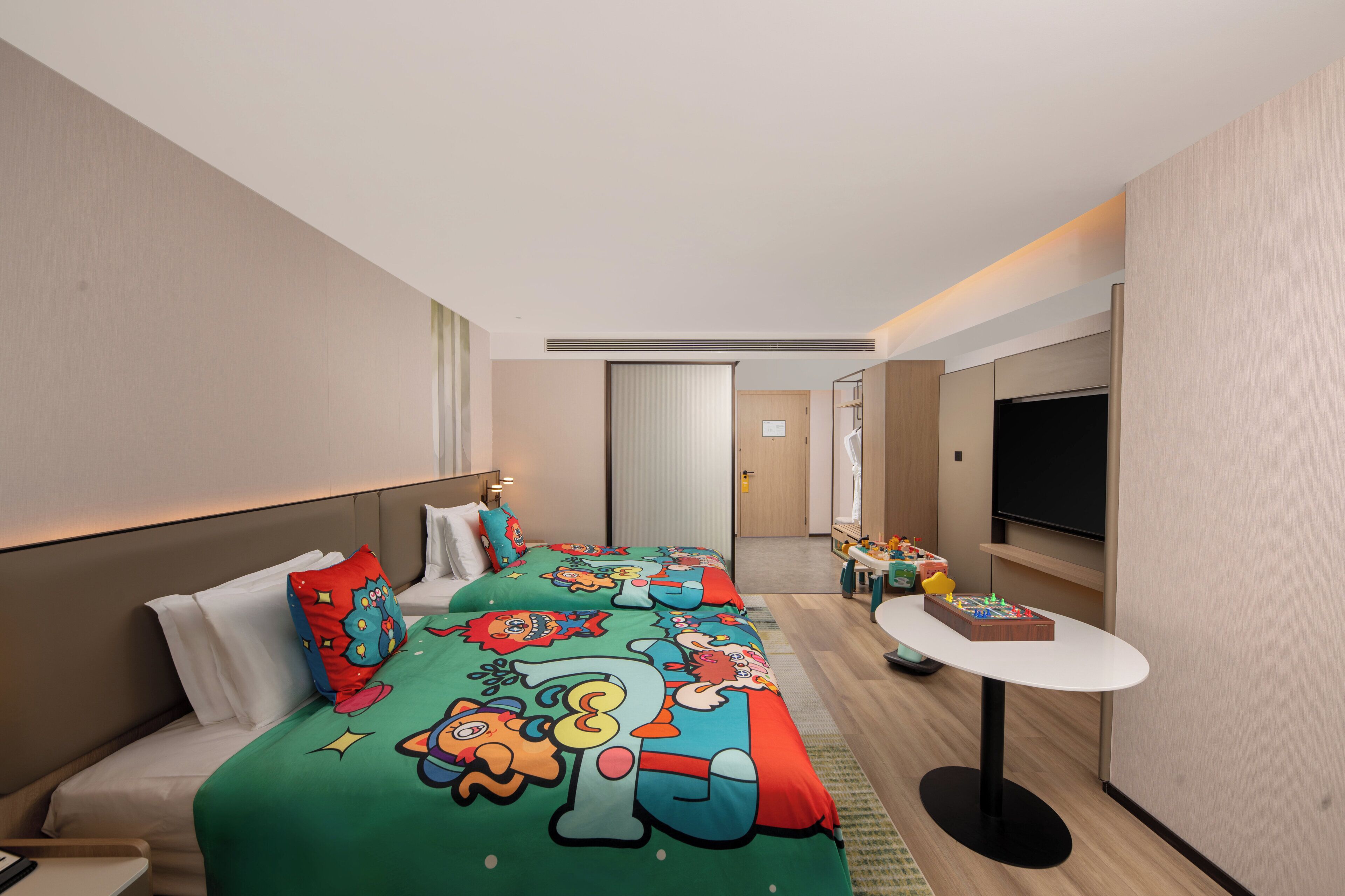 A hotel room with a large bed, a small table, a TV, and a door leading to another room.