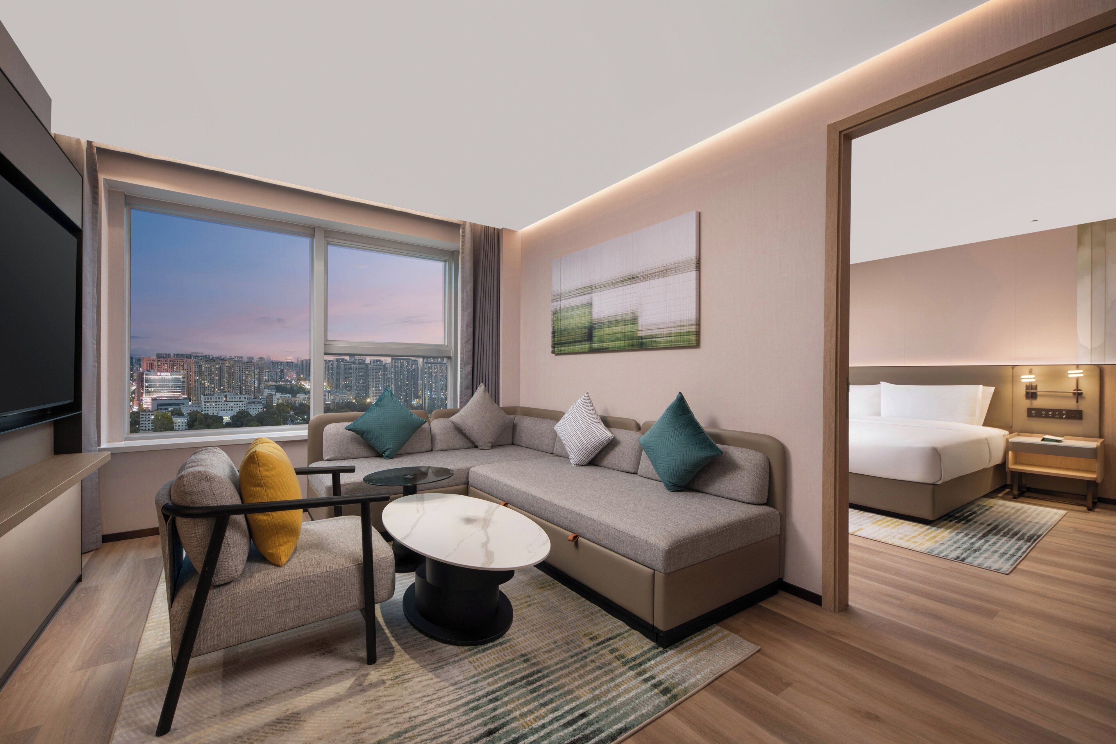 Una habitación de hotel moderna con un ventanal grande, un sofá, una mesita y una cama.