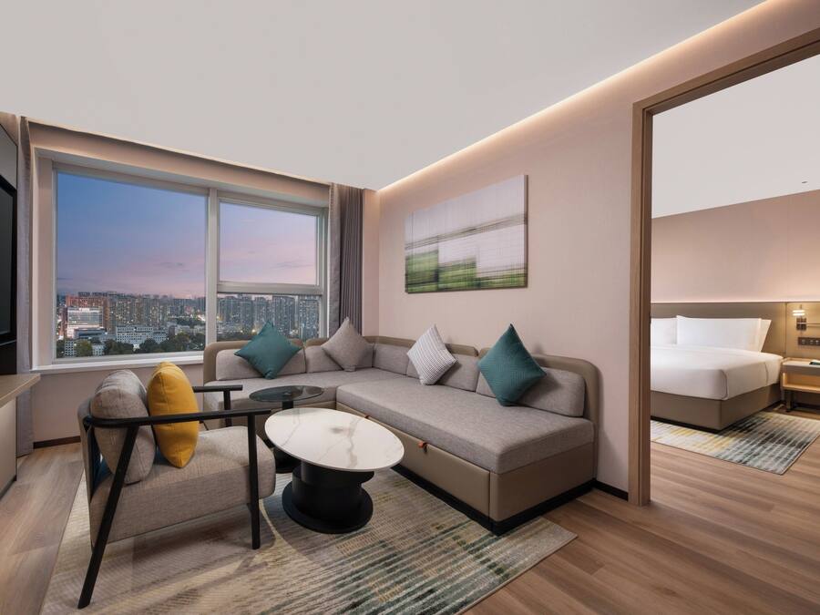 Una habitación de hotel moderna con un ventanal grande, un sofá, una mesita y una cama.