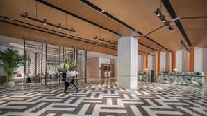 En rymlig entréhall med ett golv i geometriskt mönster, en receptionsdisk, en sittgrupp och en dekorativ växt.