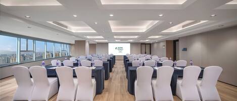 A conference room with tables and chairs, a projector screen, and a city view through large windows.