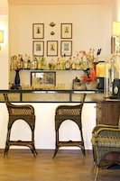 A bar area with wicker chairs, a counter with various bottles, and framed pictures on the wall.