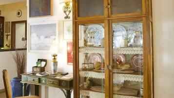 A room with a wooden cabinet with glass doors, a desk with a chair, and various framed pictures on the wall.
