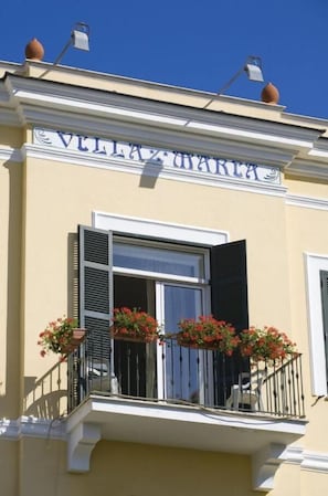 Un bâtiment doté d’un balcon, d’une fenêtre avec des volets et d’une enseigne au-dessus de la fenêtre.