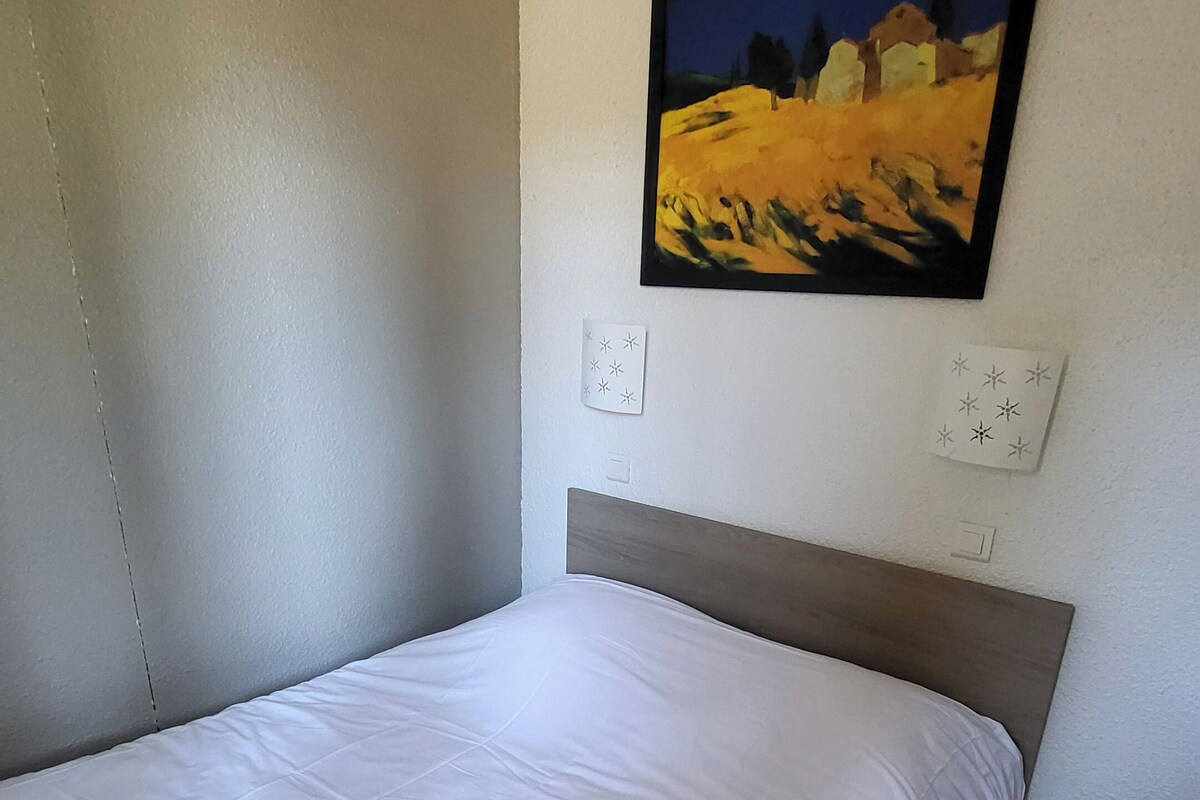 A single bed with a wooden headboard in a room with white walls and a painting above it.