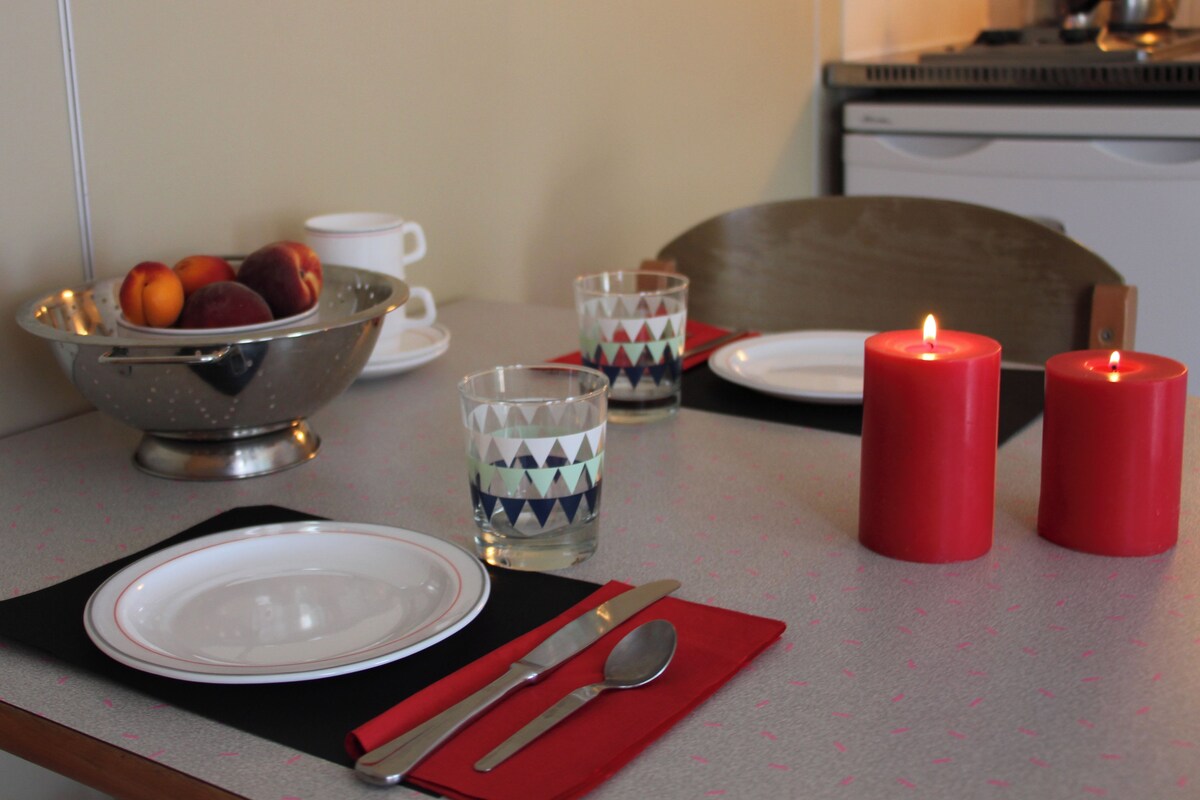 A dining table set with plates, cutlery, a bowl of fruit, glasses, and candles.