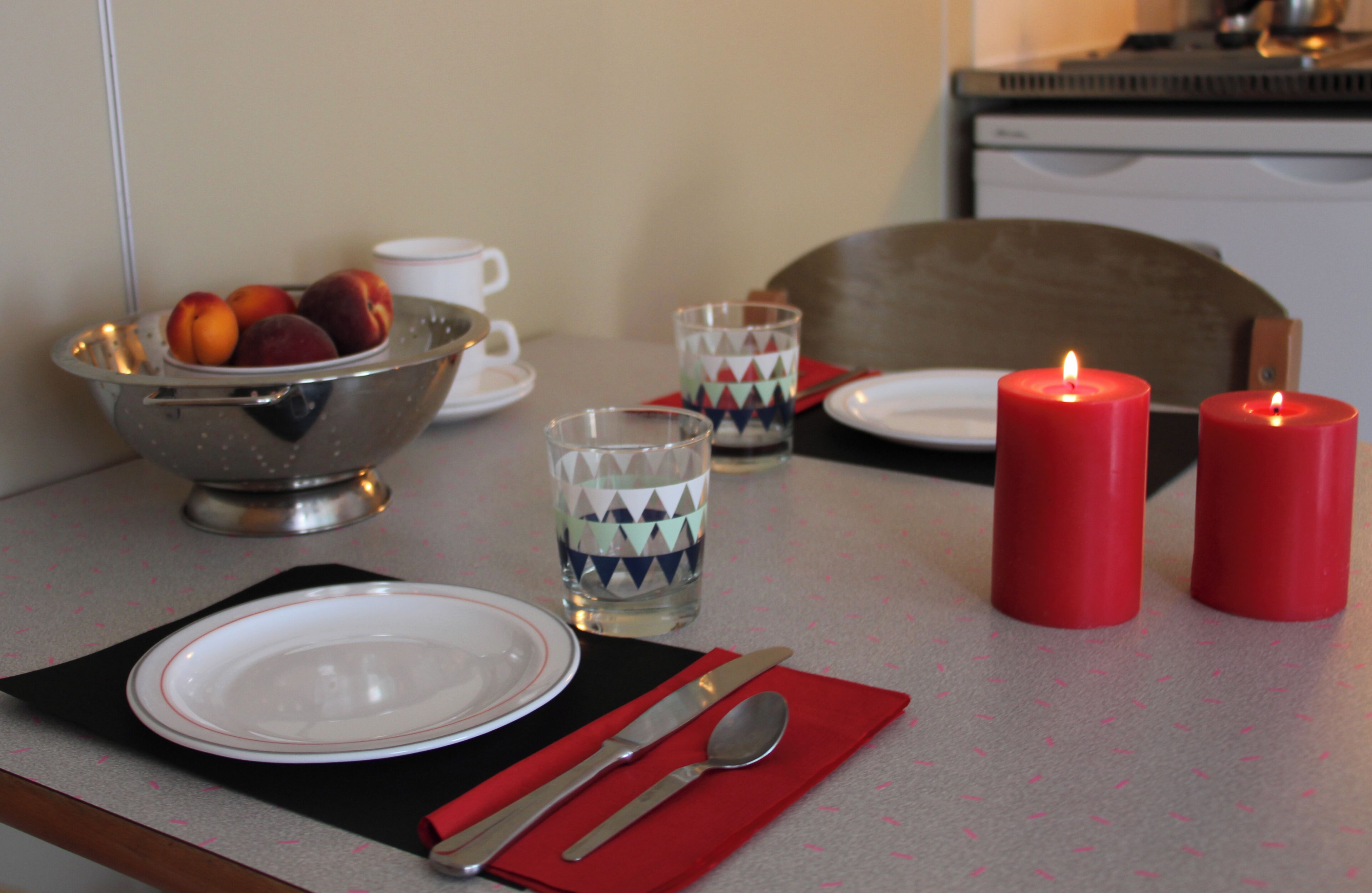 A dining table set with plates, cutlery, a bowl of fruit, glasses, and candles.
