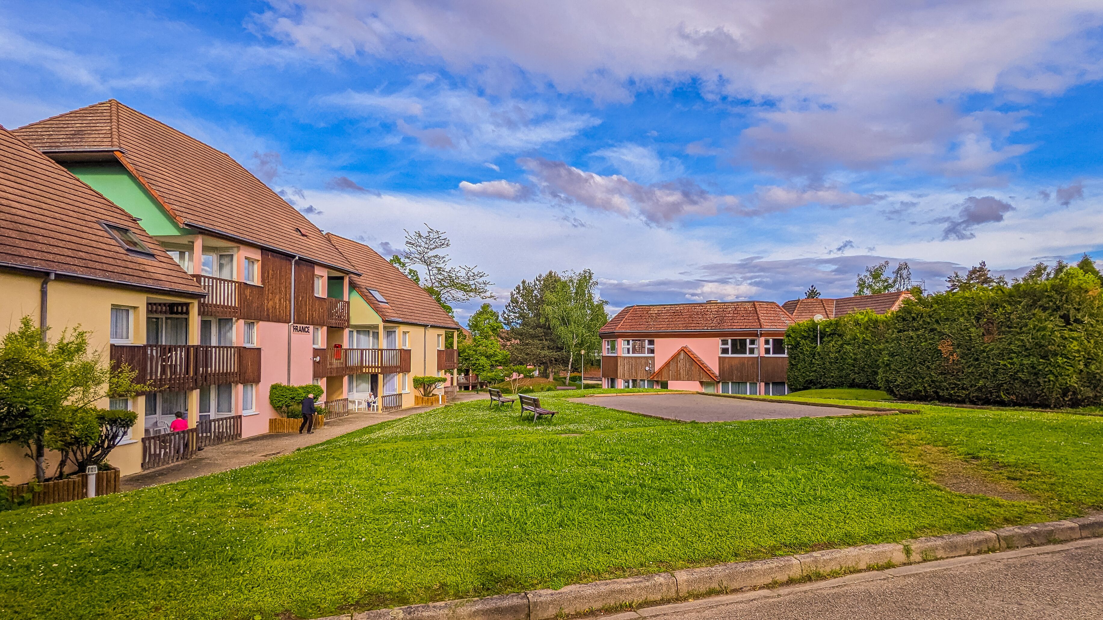 A residential area with multi-story houses, a green lawn, and a clear sky.