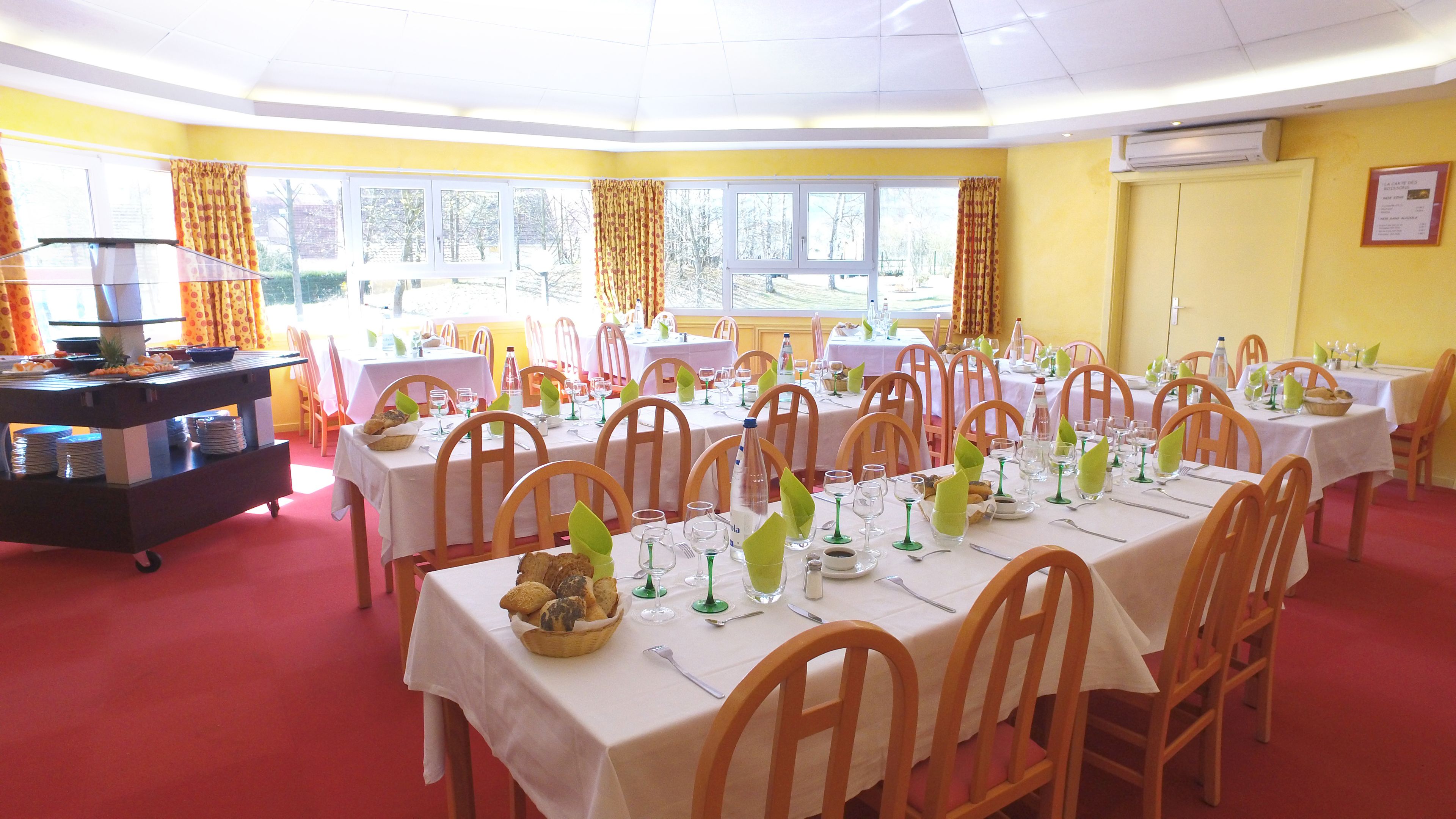 A dining area with multiple tables set for guests, featuring white tablecloths and wooden chairs.