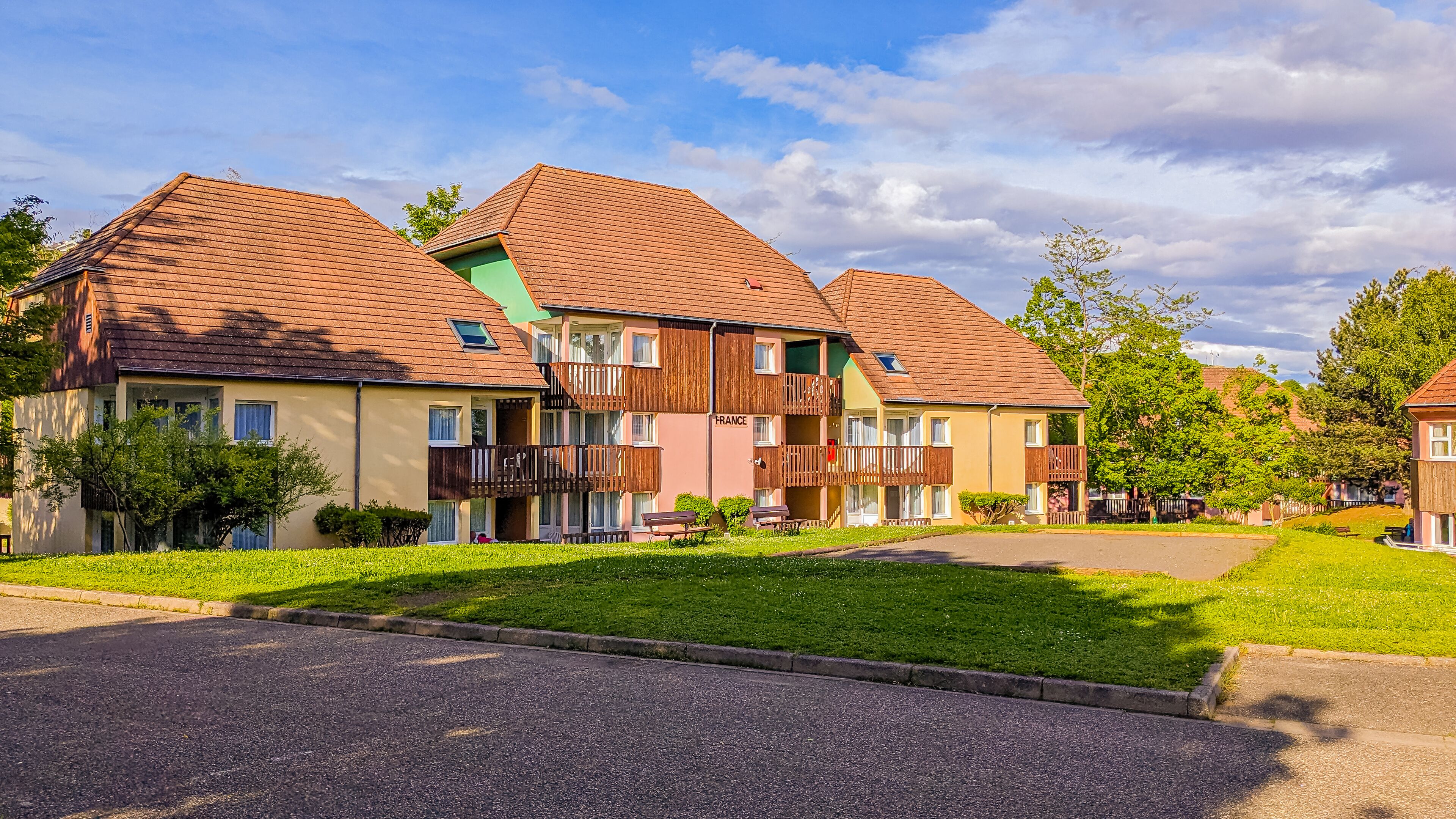 A row of multi-story residential buildings with sloped roofs, balconies, and a well-maintained lawn in front.