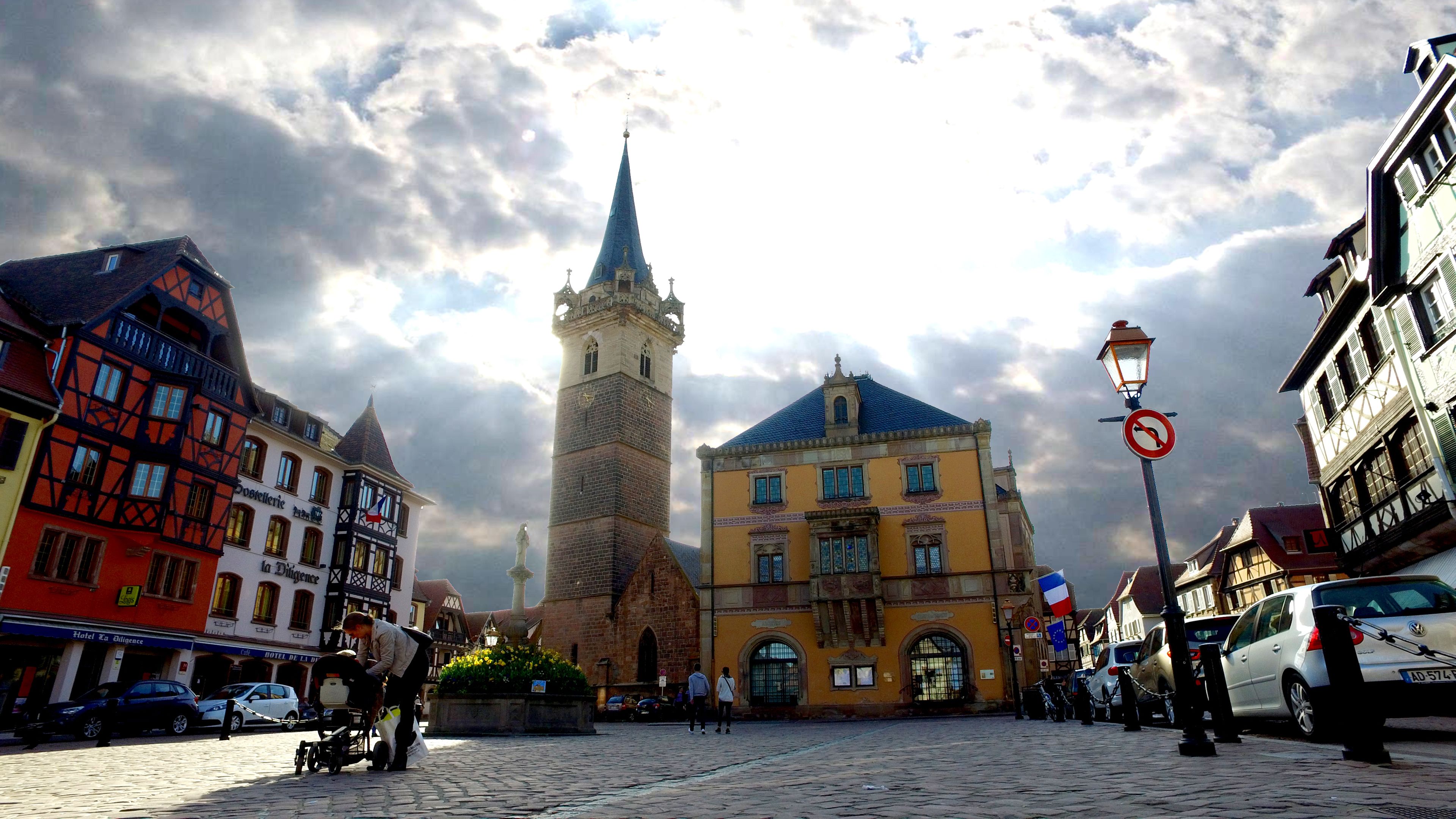 A cobblestone square with historic buildings, a prominent tower, and a fountain.