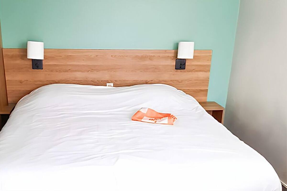 A neatly made bed with white sheets and a single orange item on the bed.