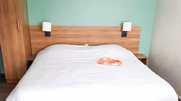 A neatly made bed with white sheets and a single orange item on the bed.