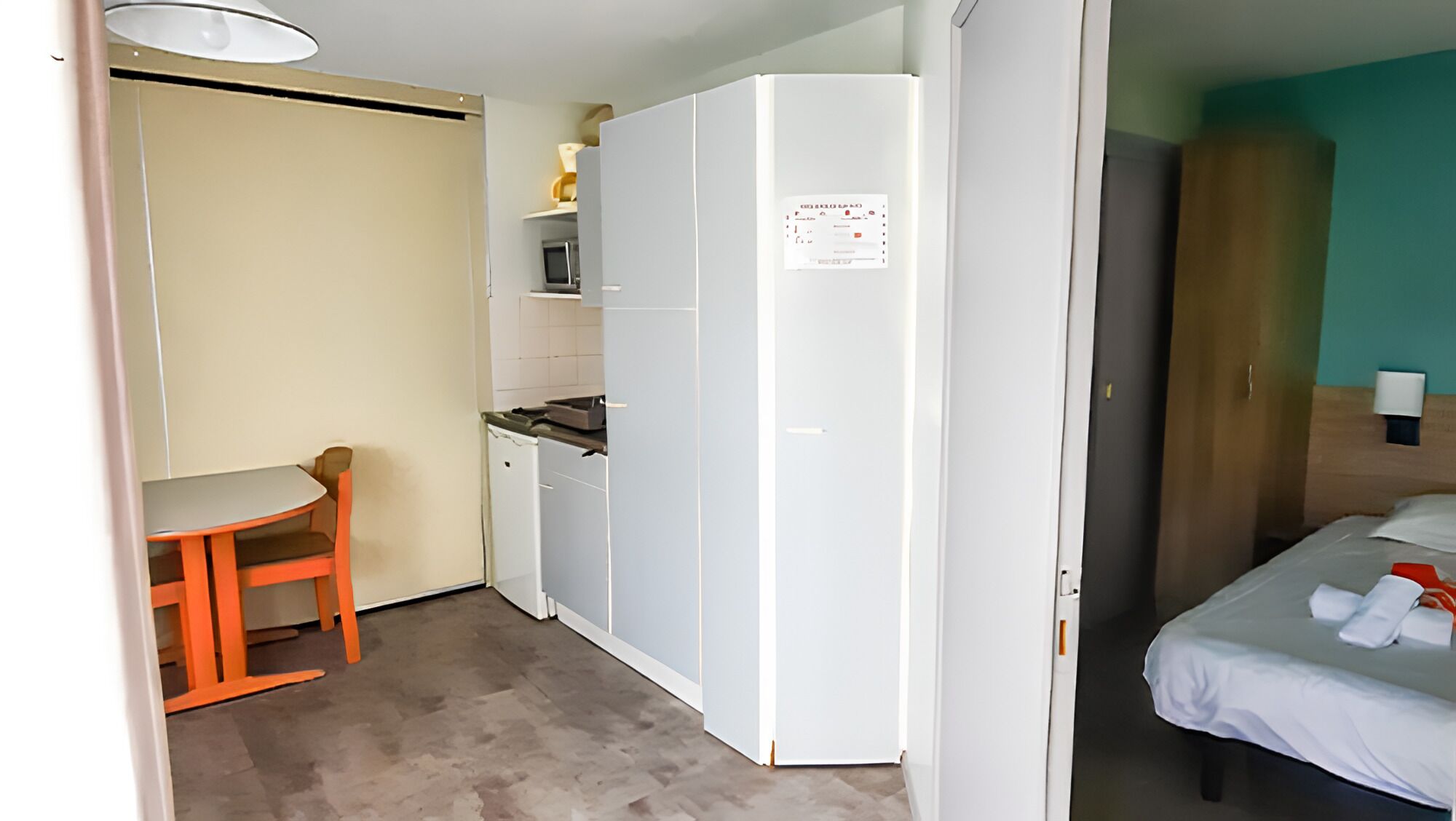 A compact room with a kitchenette, a dining area, and a bed.