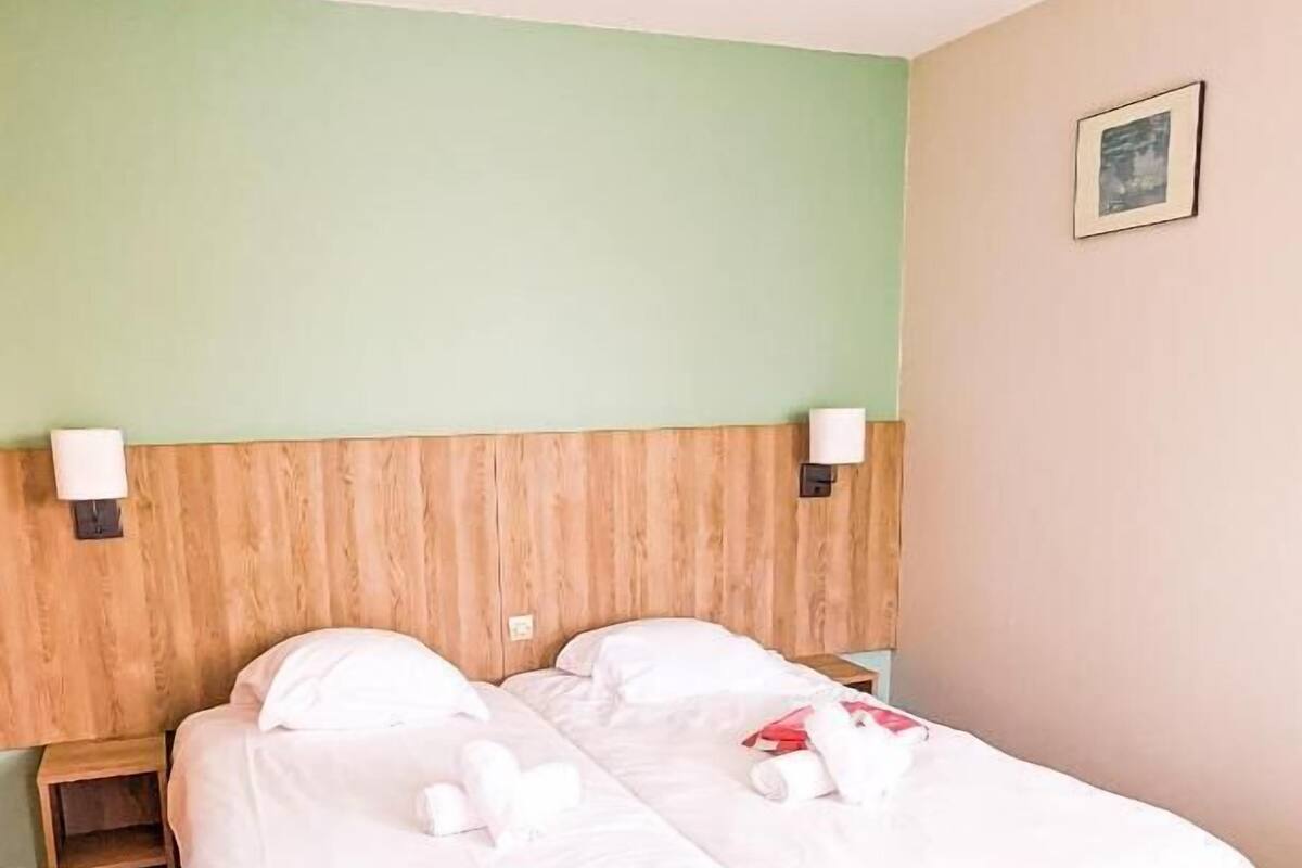 A double bed with white bedding in a room with green walls and a wooden headboard.