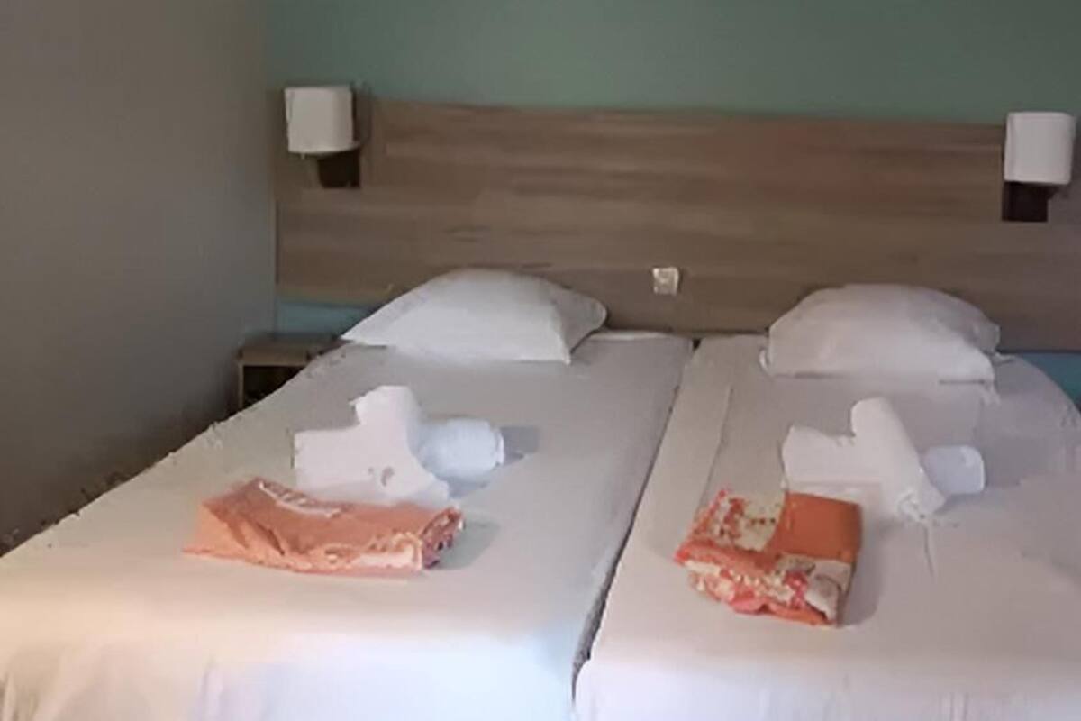 A double bed with white linens, two pillows, and two folded towels.
