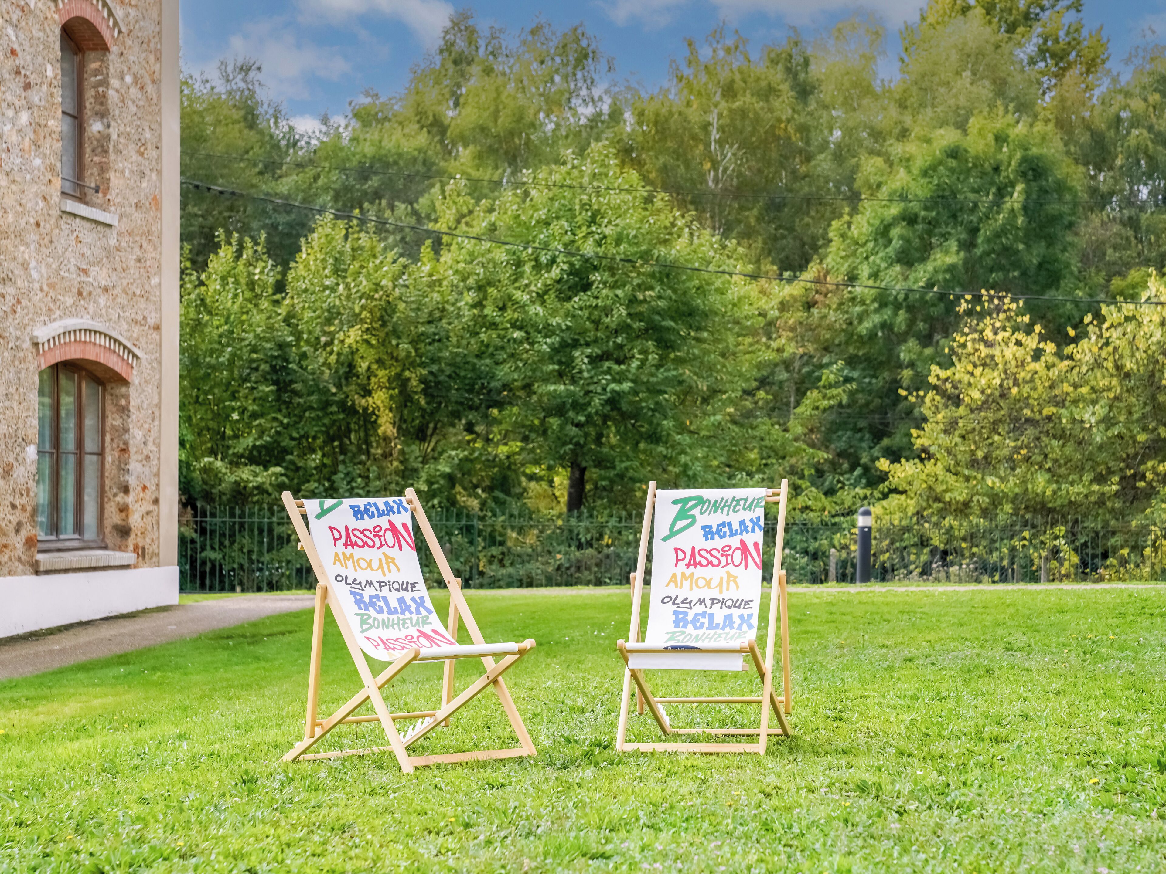 Deux chevalets en bois, chacun portant une affiche, sont placés dans une zone herbeuse, avec un bâtiment en pierre en arrière-plan.