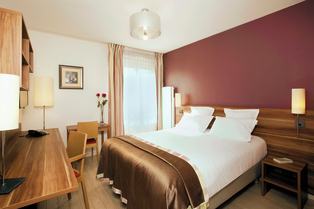 A hotel room with a bed, bedside tables, a desk, a chair, a lamp, a picture on the wall, and a window with curtains.