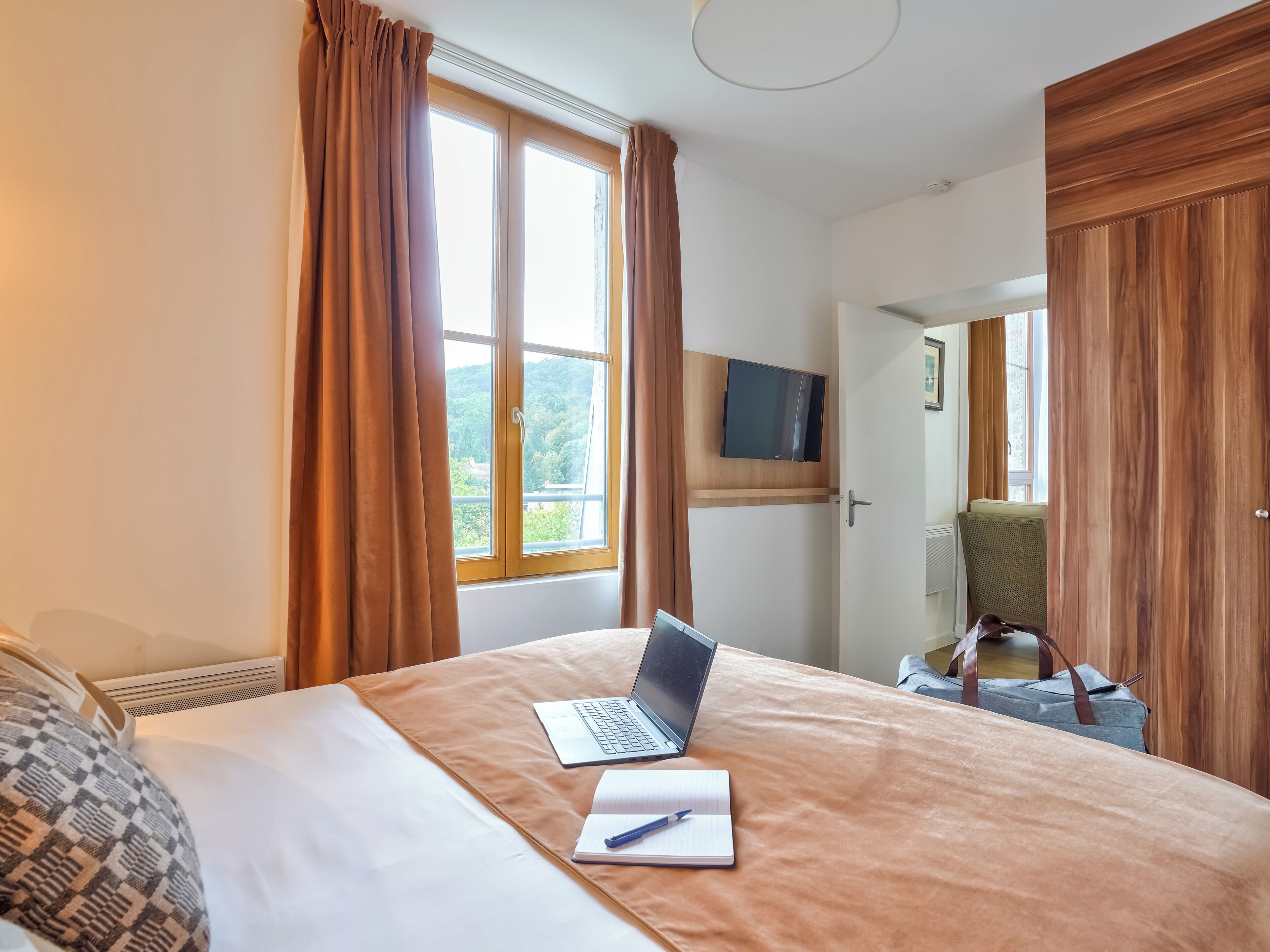 A hotel room with a bed, a laptop, a notebook, and a chair.