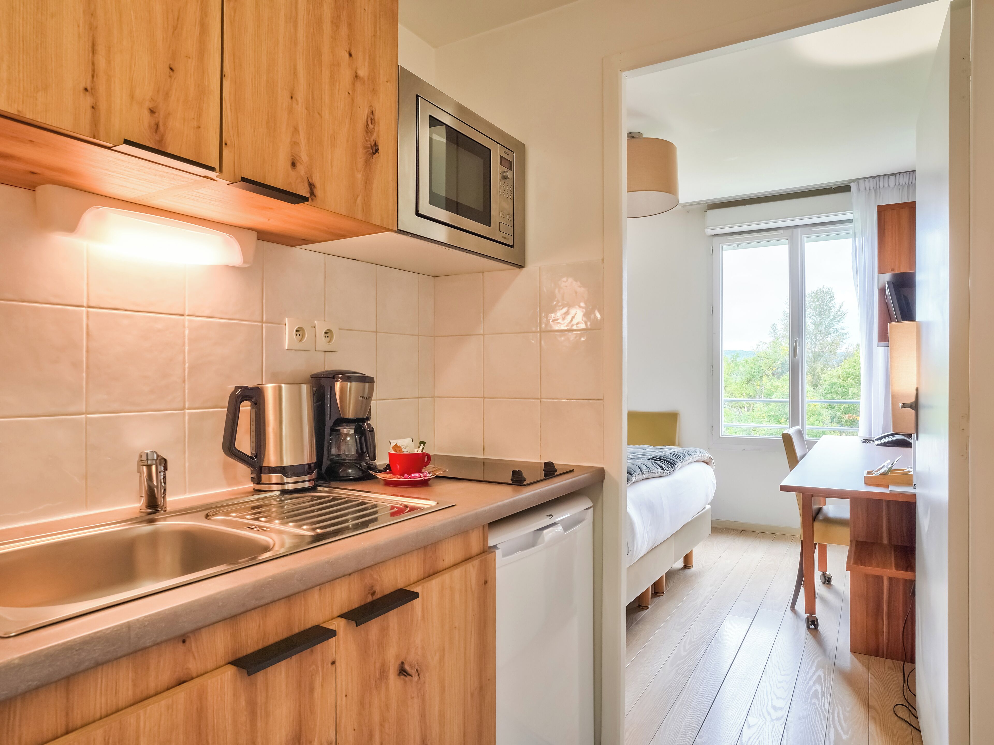 Une cuisine moderne avec des meubles en bois, un évier en acier inoxydable, une machine à café et un four à micro-ondes.