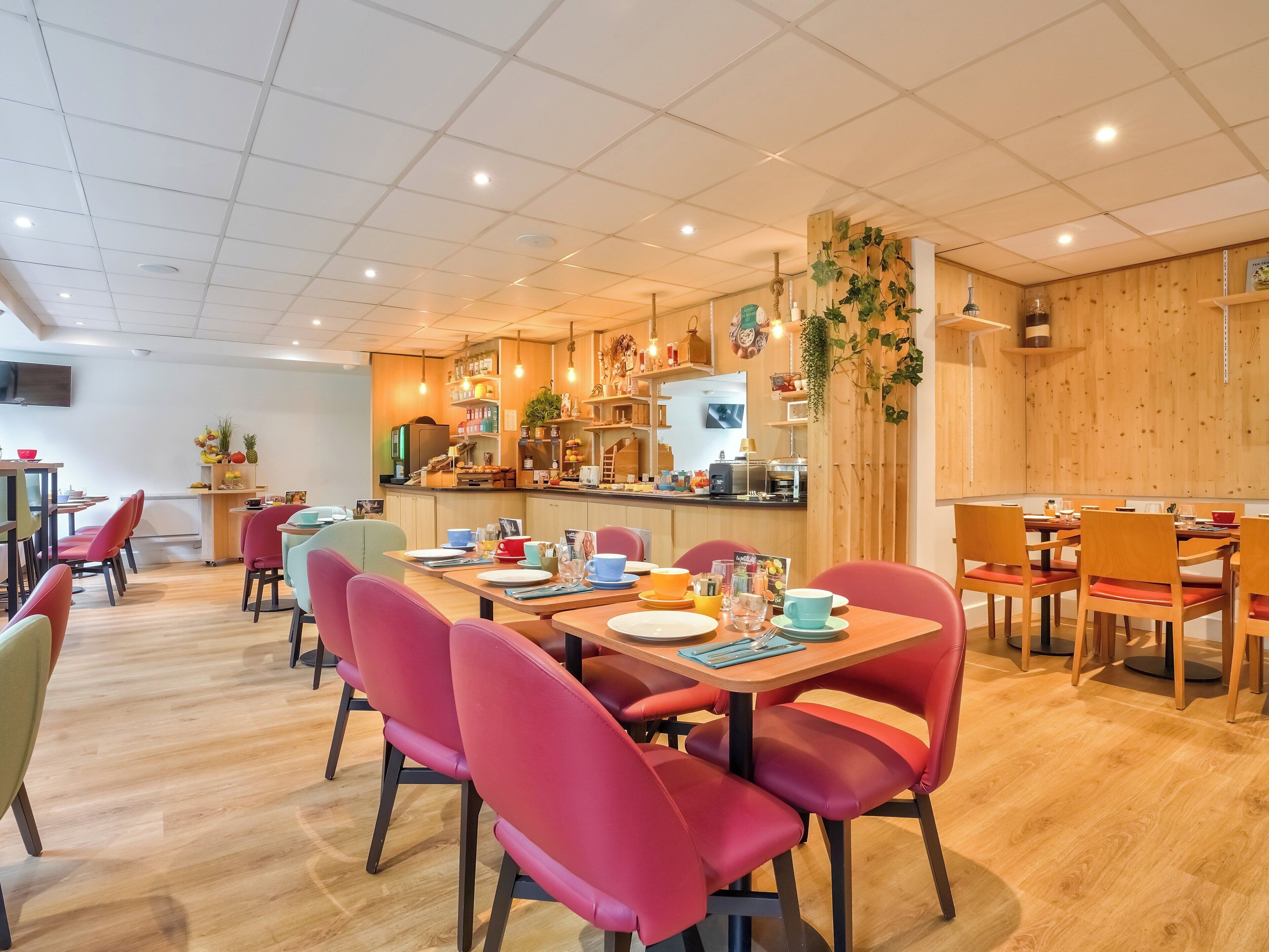 Een modern restaurant met houten vloeren, rode beklede stoelen en een bar in het midden.