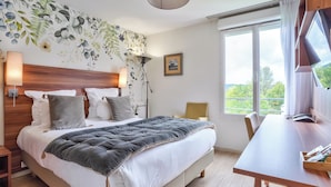 A neatly arranged bedroom with a large bed, bedside lamps, a wooden headboard, a desk, and a window with a view.