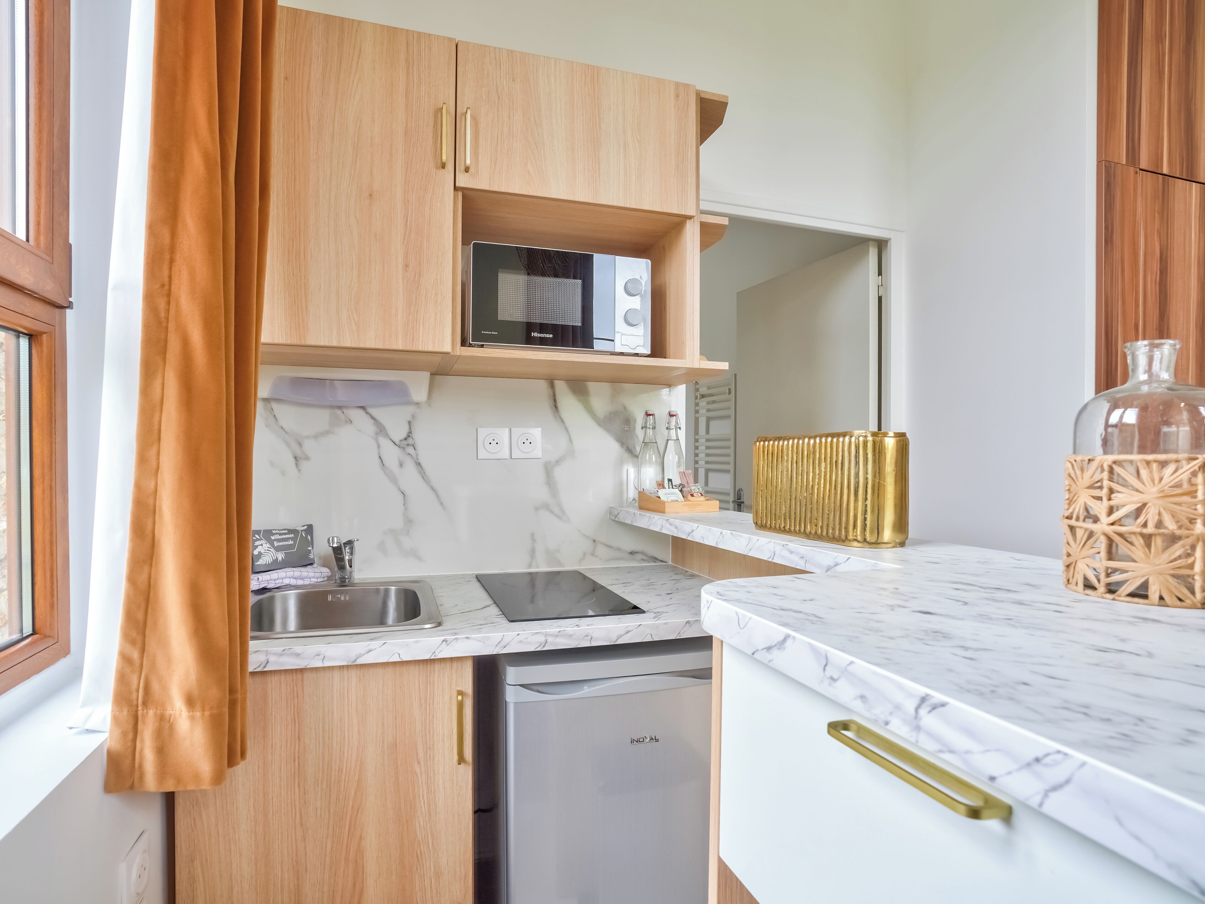 A compact kitchen with wooden cabinets, a built-in microwave, a dishwashing unit, and a marble countertop.
