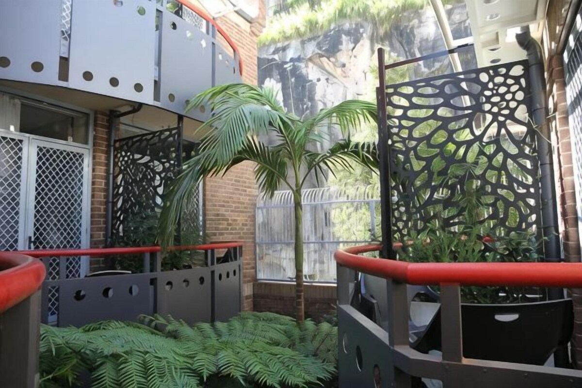Un balcon agrémenté d’un palmier, d’une grille en métal décorative et d’une rambarde rouge.