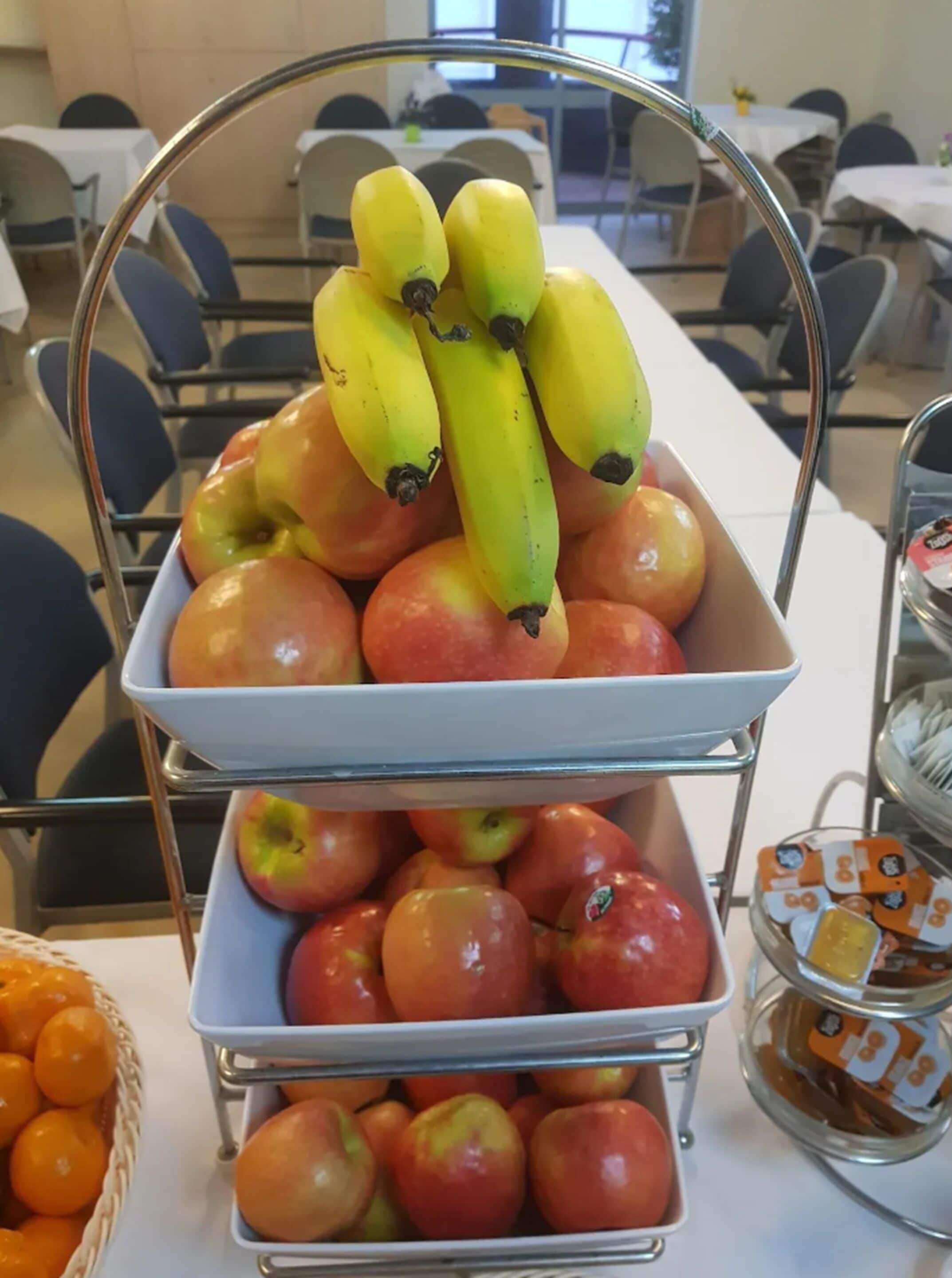 Ein dreistöckiger Obststand mit Äpfeln und Bananen in einem Konferenzraum mit Tischen und Stühlen.