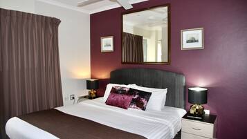 A hotel room with a bed, two bedside tables, a ceiling fan, a large mirror, and two framed pictures on the wall.