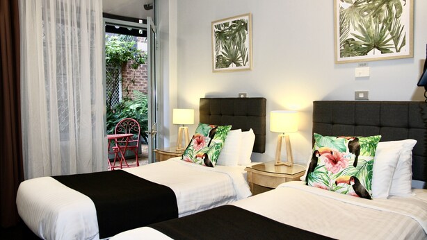 A hotel room with two beds, a large window with curtains, a small table, and two nightstands with lamps.