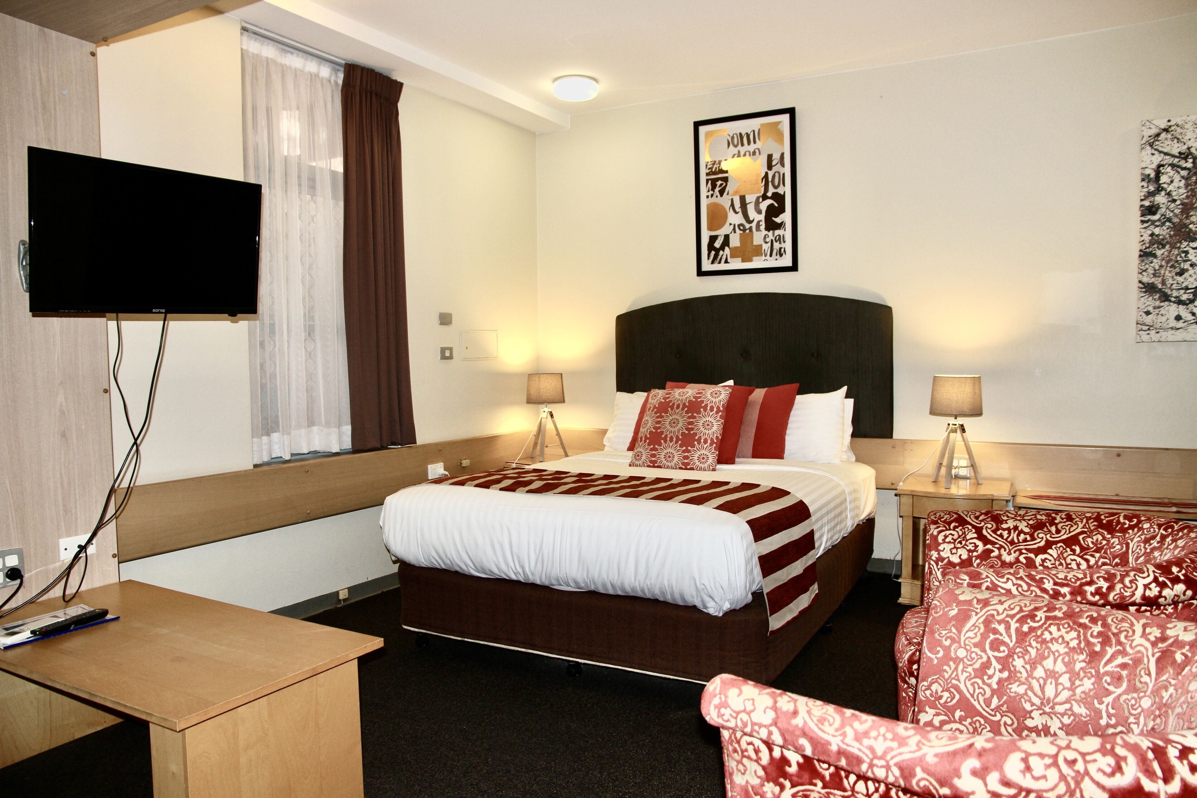 Une chambre d’hôtel avec un lit, un téléviseur fixé au mur, un bureau et une chaise.