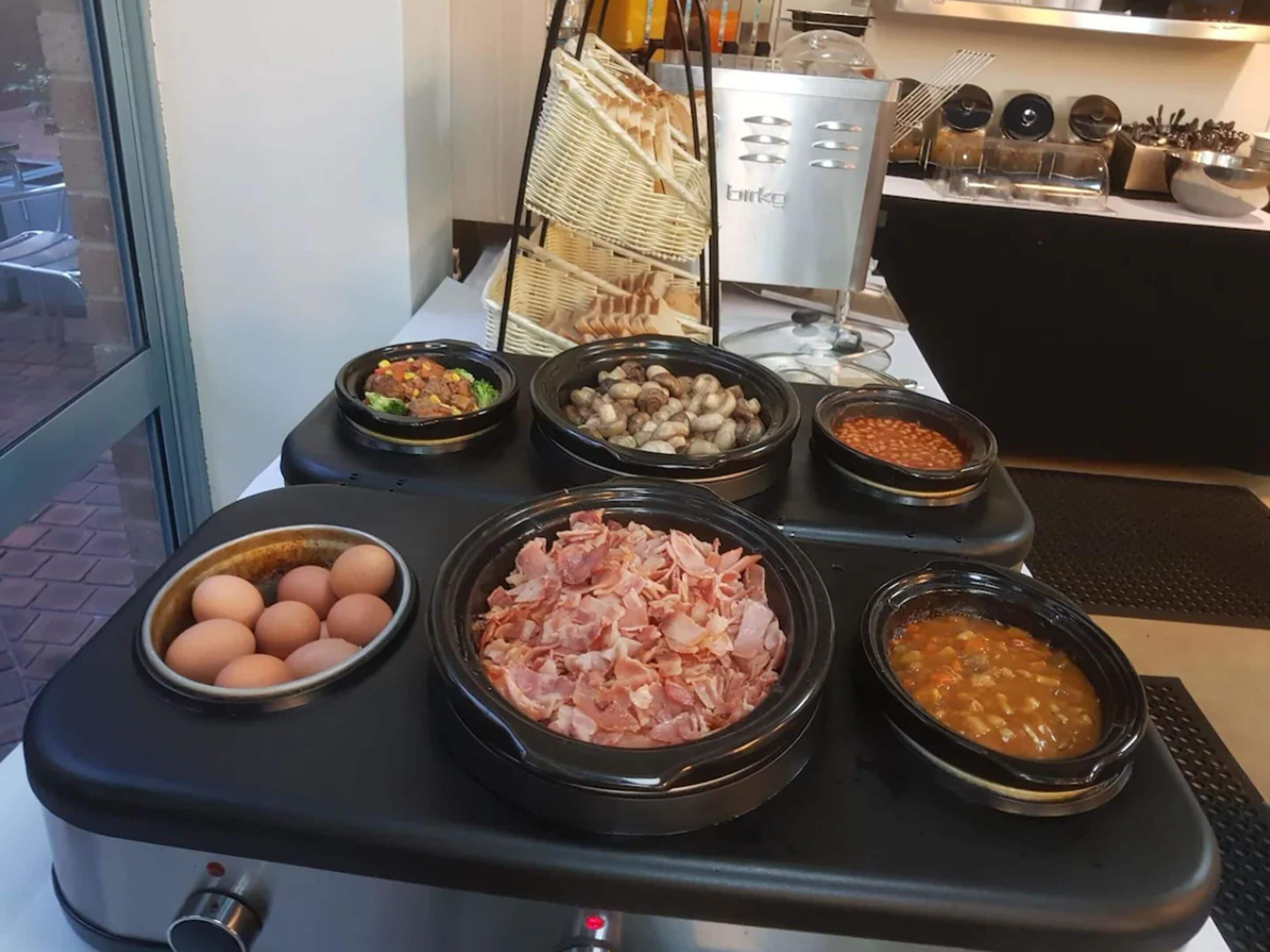 A buffet table with various food items including eggs, ham, beans, and vegetables.