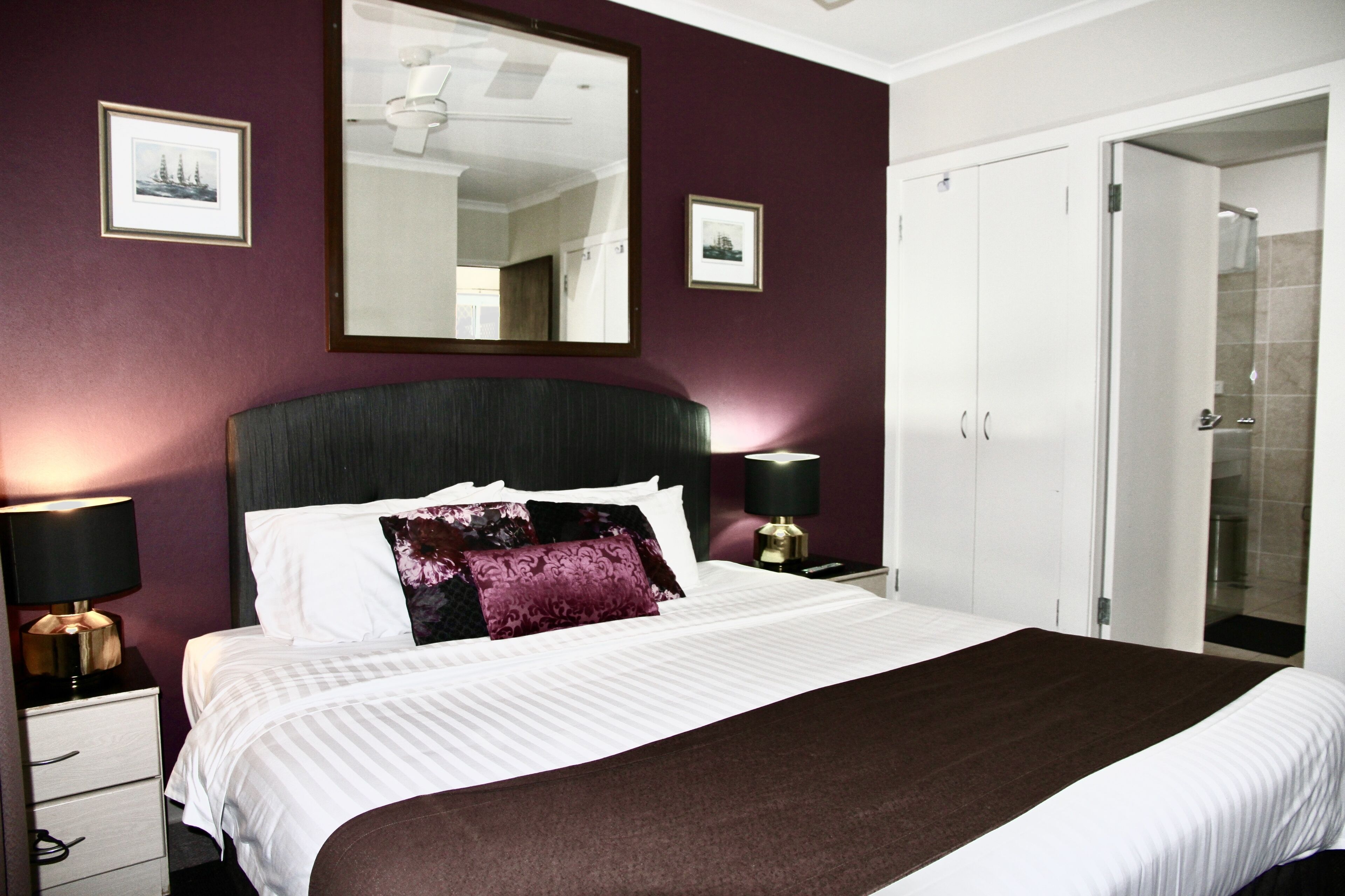 A neatly made bed with a headboard, two bedside lamps, and a large mirror above the bed.
