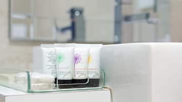 A bathroom with a glass shelf holding three tubes of Coway shower gel and conditioner, and a white bottle on the left.