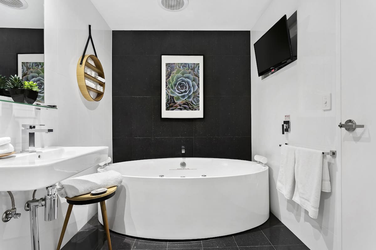 A modern bathroom with a freestanding bathtub, a large mirror, a wall-mounted TV, and a framed succulent artwork.