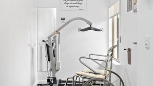 Habitación accesible en silla de ruedas con una camilla de exploración médica, aire acondicionado de pared y una puerta con ventana.