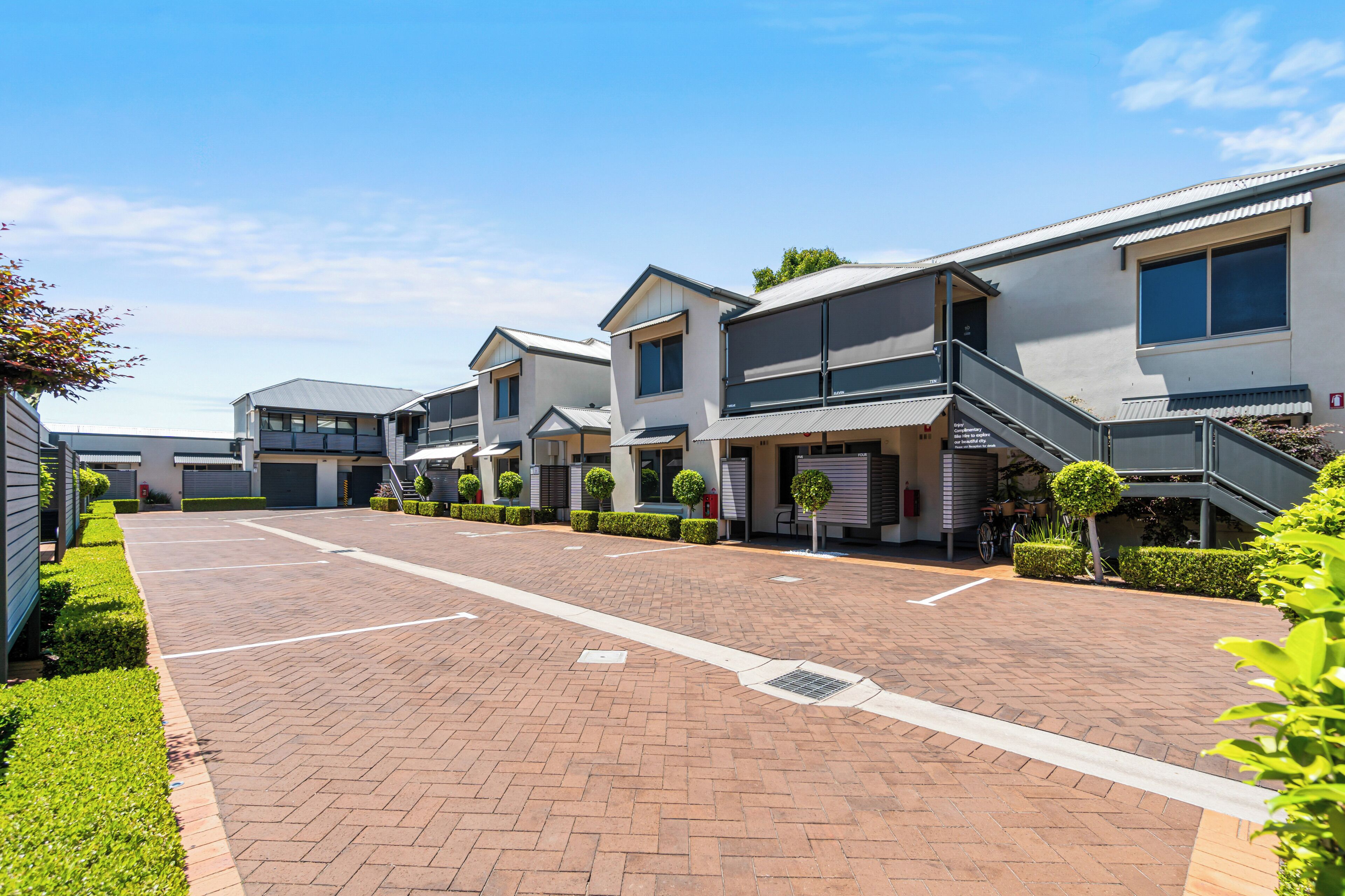 Un moderno complejo residencial con varias casas de dos pisos, un camino pavimentado y jardines bien cuidados.