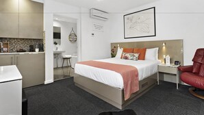Una habitación de hotel moderna con cama, escritorio, silla, una kitchenette pequeña y baño.