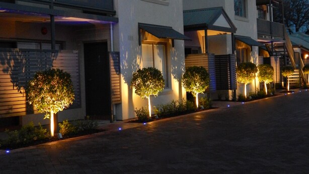 Un edificio residencial moderno con varios pisos, balcones e iluminación destacada en la entrada.