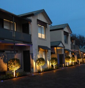 Un edificio residencial moderno con varios pisos, balcones e iluminación destacada en la entrada.