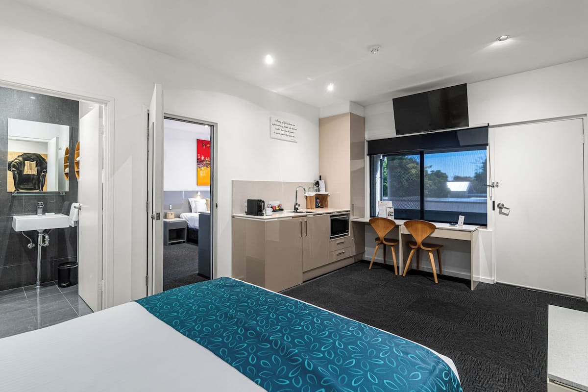 A hotel room with a bed, a desk, a chair, a TV, a window, a sink, and a mirror.