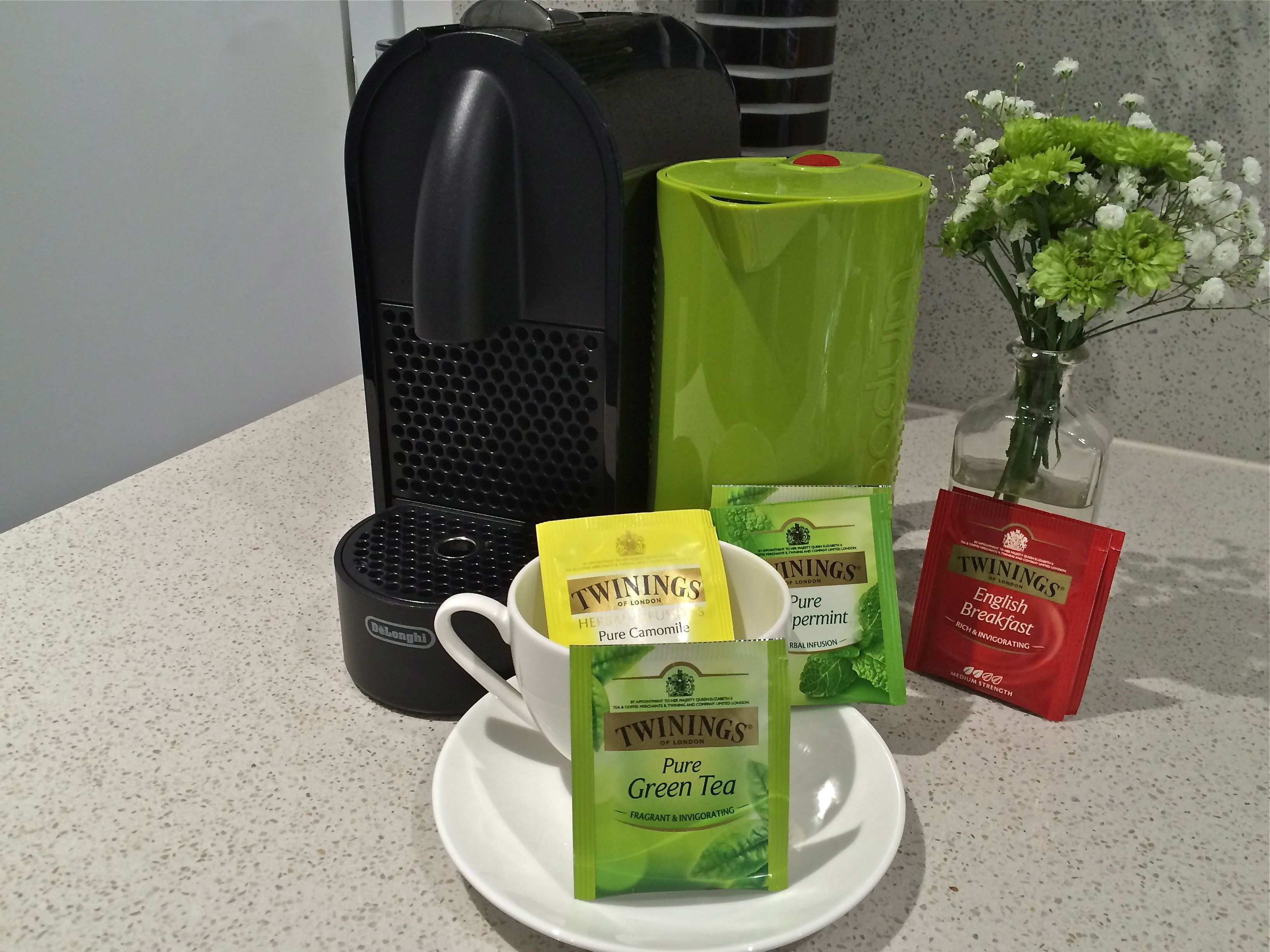 Una encimera de cocina con una cafetera, un sobre de té verde y un sobre de té rojo.