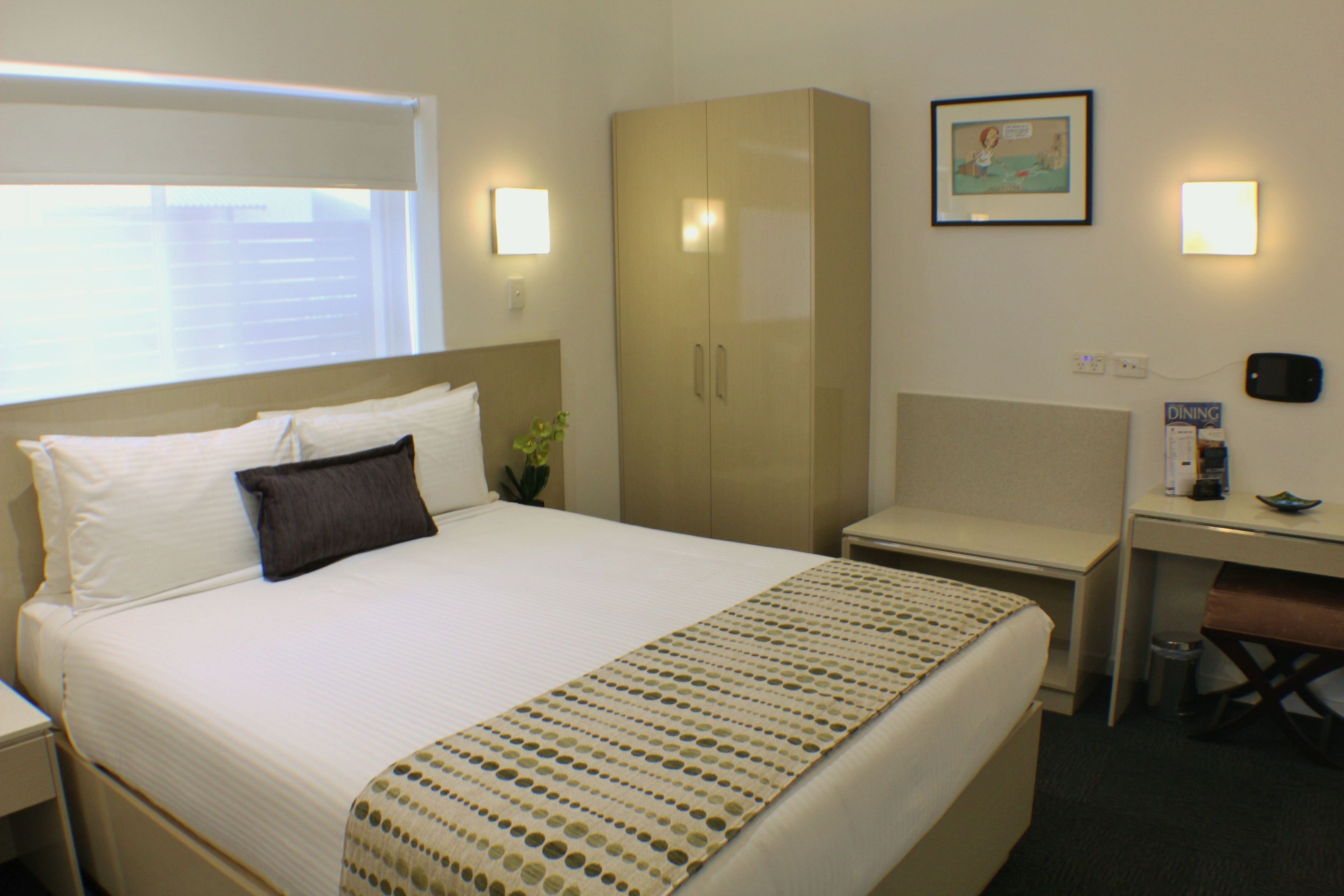 A hotel room with a bed, a desk, a wardrobe, and a dining area.