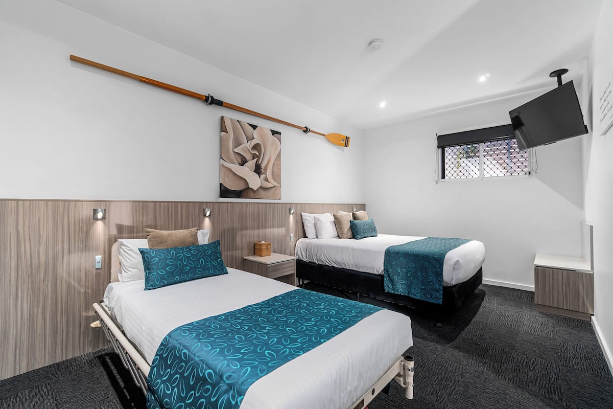 A hotel room with two beds, a wooden headboard, a mounted television, and a window with a view.