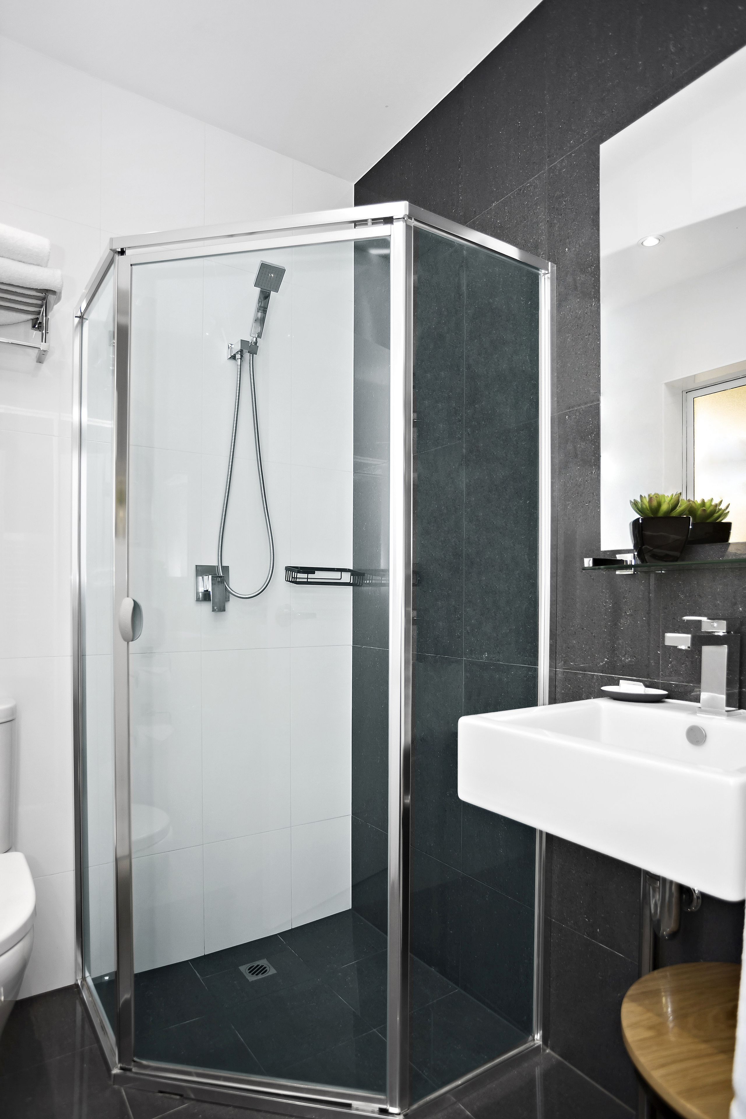 A modern bathroom with a glass-enclosed shower, a white sink, and a dark tiled wall.